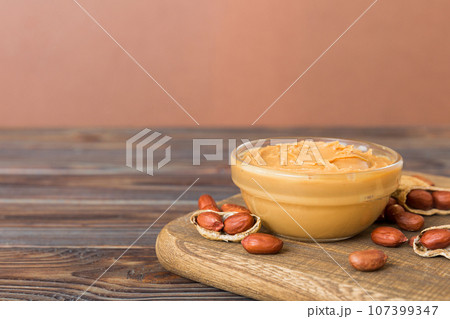 Bowl of peanut butter and peanuts on table background. top view with copy space. Creamy peanut pasta in small bowl Bowl of peanut butter and peanuts on table background. top view with copy space. Creamy peanut pasta in small bowl 107399347