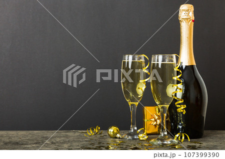 Champagne bottle with confetti, glasses and christmas decor on colored holiday background. Flat lay New Year decorations Champagne bottle with confetti, glasses and christmas decor on colored holiday background. Flat lay New Year decorations 107399390