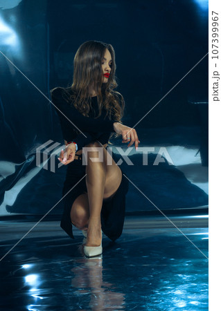 Sexy fashionable lady in black dress posing in studio on dark foil background 107399967