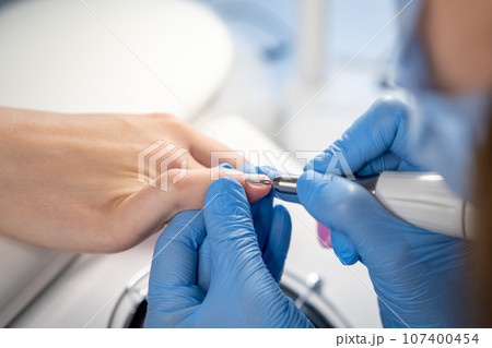 Nail care procedure in a beauty salon. Female hands and tools for manicure, process of performing manicure in beauty salon. Concept spa body care. Gloved hands of a skilled manicurist cutting cuticles 107400454