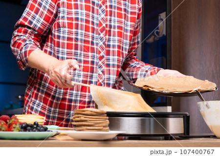 Woman cooking delicious crepe on electric pancake maker in kitchen, closeup Woman cooking delicious crepe on electric pancake maker in kitchen, closeup 107400767