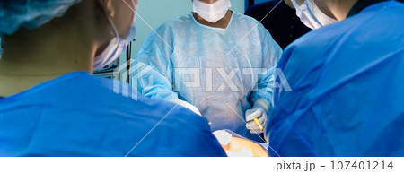 A team of surgeons in blue sterile gowns performs a surgical operation. A team of surgeons in blue sterile gowns performs a surgical operation. 107401214
