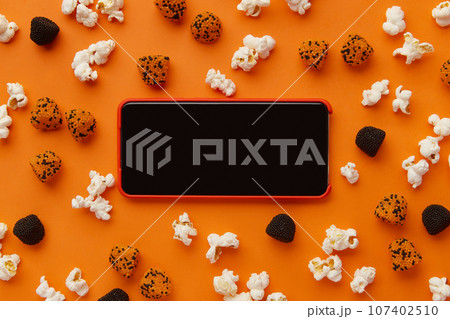 Smartphone, box of popcorn and gummies on an orange background 107402510