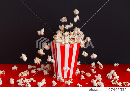 Striped box with popcorn on a red and black background Striped box with popcorn on a red and black background 107402533