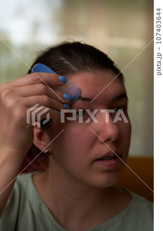 Woman is massaging her face scraper gua sha. Woman is massaging her face scraper gua sha. 107403644