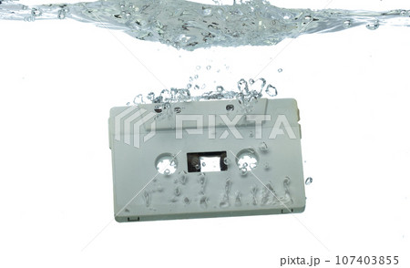 Cassette retro vintage Tape fall into clear water with air bubble. Black retro vintage cassette magnetic tape drop to wash old time. White background isolated freeze element 107403855