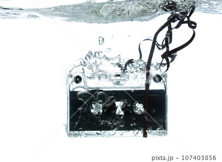 Cassette retro vintage Tape fall into clear water with air bubble. Black retro vintage cassette magnetic tape drop to wash old time. White background isolated freeze element 107403856