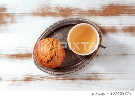 Orange muffin with tea on a rustic wooden kitchen table, on a vintage tray Orange muffin with tea on a rustic wooden kitchen table, on a vintage tray 107405778