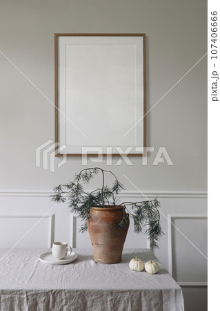 Elegant interior, Christmas table setting decor. Winter art composition. Blank wooden picture frame mockup hanging on beige wall. Pine tree branches in vase. Cup of coffee, white pumpkins. Vertical. Elegant interior, Christmas table setting decor. Winter art composition. Blank wooden picture frame mockup hanging on beige wall. Pine tree branches in vase. Cup of coffee, white pumpkins. Vertical. 107406666