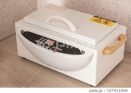 Electric sterilizer for manicure and medical devices. Mini high temperature sterilizer close up. Packing manicure tools kraft paper bag for for further sterilization. Cleanliness and disinfection 107411000