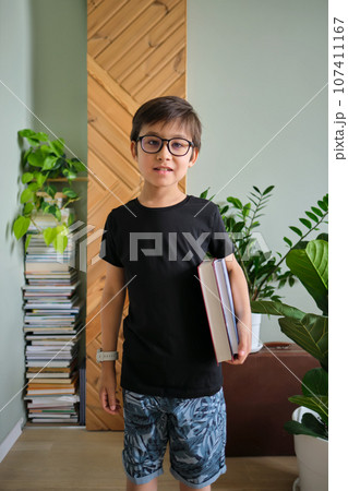 A boy holds a stack of books against the background home library. 107411167