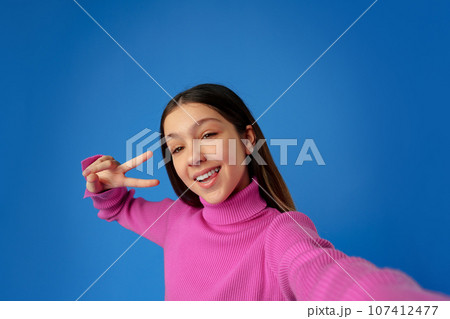 Portrait of a smiling teen girl making selfie photo on blue background Portrait of a smiling teen girl making selfie photo on blue background 107412477