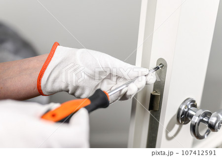 a man in white gloves holds a screwdriver and tightens the lock. 107412591
