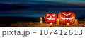 a pair of halloween pumpkin lanterns sitting on a sandy beach at night. 107412613