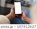 female user holding smartphone in hands, mobile phone white blank screen mockup, using mobile apps at home. 107412627