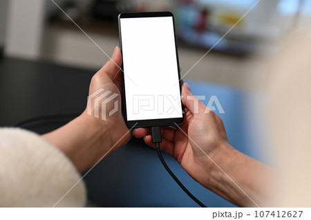 female user holding smartphone in hands, mobile phone white blank screen mockup, using mobile apps at home. 107412627