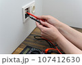 An electrical technician measures voltage using a multimeter tester. Measuring voltage in a socket. 107412630