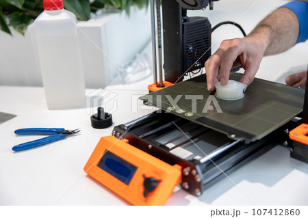Modern 3D printer equipment and man working with it in office. Modern 3D printer equipment and man working with it in office. 107412860