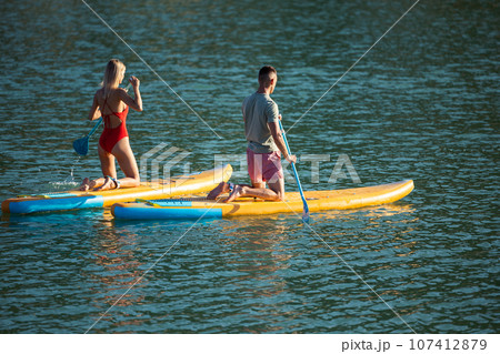Woman and man surfing in ocean on sup board ar summer vacation. Woman and man surfing in ocean on sup board ar summer vacation. 107412879