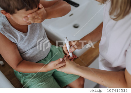 Mother checking her son's blood glucose level at home using a fingerstick glucose meter. 107413532