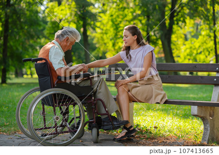 A young caregiver spending quality time with lonely senior client in the city park. 107413665