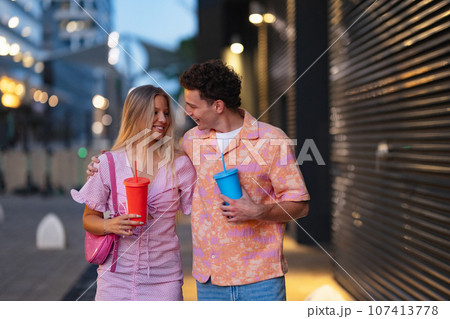 Gen Z couple in pink outfits leaving the cinema with drinks in hand. Gen Z couple in pink outfits leaving the cinema with drinks in hand. 107413778