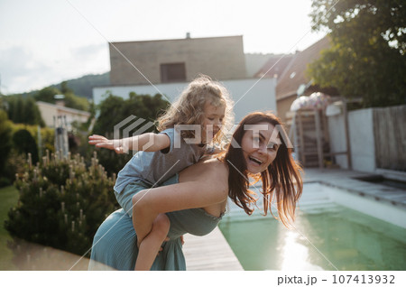 The mom is giving her little boy a piggyback ride in the garden. 107413932