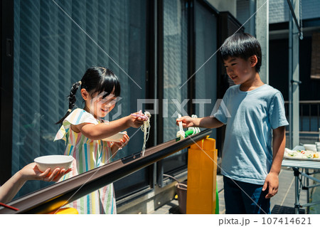 お庭で雨どい流しそうめんをする家族 107414621