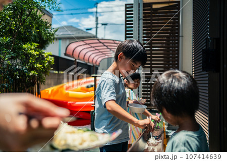 お庭で雨どい流しそうめんをする家族 107414639