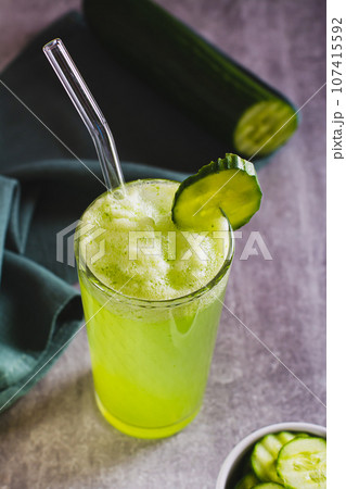 Detox cucumber lemonade in a glass with a straw and a cucumber on the table vertical view 107415592