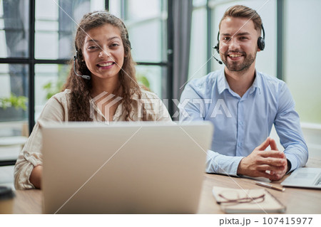 smilling man and charming woman are sitting at laptops in headphones smilling man and charming woman are sitting at laptops in headphones 107415977