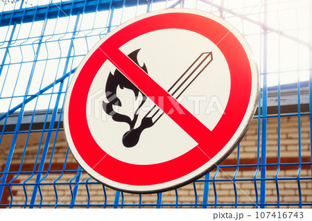 Sign prohibiting starting fire hangs on metal fence. Fire hazardous object. Crossed match 107416743