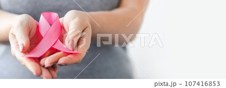 Woman in gray t-shirt holds pink ribbon in her hands. Breast Cancer Awareness Month. Supporting and promoting campaign against cancer. 107416853