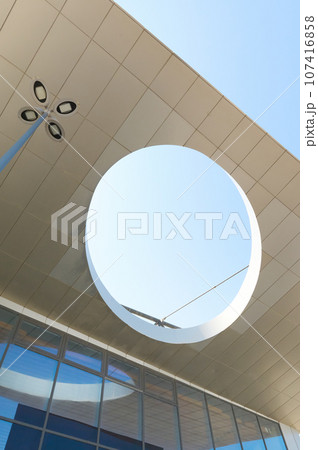Bottom view of a round element of modern office building's design against blue sky background. Upgrowing perspective. 107416858