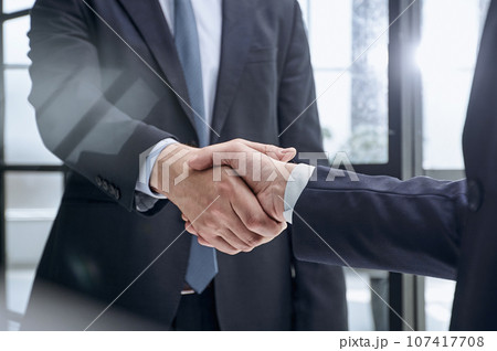 executives shaking hands in front of their manager and a colleague 107417708