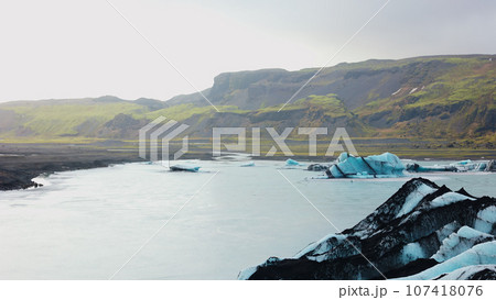 Natural vatnajokull icebergs with blocks of ice, massive icy land in nordic landscapes and scenery. Diamond shape glacier with frozen water near mountains with frost. Handheld shot. Natural vatnajokull icebergs with blocks of ice, massive icy land in nordic landscapes and scenery. Diamond shape glacier with frozen water near mountains with frost. Handheld shot. 107418076