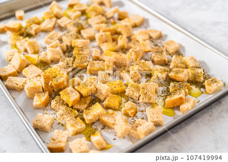 Baking croutons seasoned with olive oil and spiced on a baking sheet lined with parchment paper. Baking croutons seasoned with olive oil and spiced on a baking sheet lined with parchment paper. 107419994