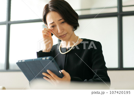 タブレット端末を見る喪服の女性 107420195