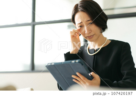 タブレット端末を見る喪服の女性 107420197