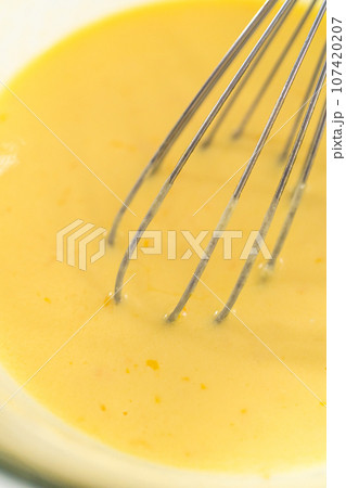 Mixing wet ingredients in a large glass mixing bowl to bake mini Easter bread kulich. 107420207