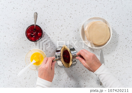 Flat lay. Filling empanada dough with cherry pie filling to make sweet cherry empanadas in the air fryer. Flat lay. Filling empanada dough with cherry pie filling to make sweet cherry empanadas in the air fryer. 107420211