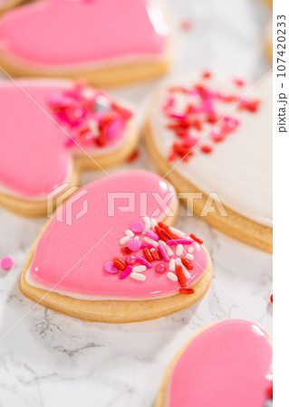 Decorating heart-shaped sugar cookies with pink and white royal icing for Valentine's Day. 107420233