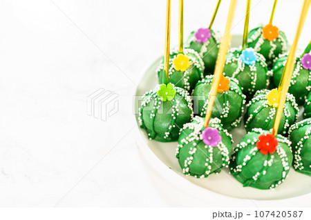 Cactus-shaped cake pops, beautifully decorated with luster dust, sugar flowers, and white sprinkles, arranged in celebration of Cinco de Mayo. 107420587