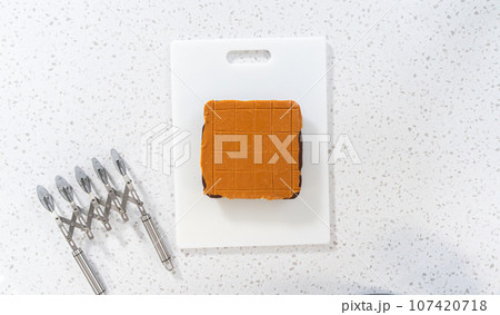 Flat lay. Scoring caramel fudge using a wheel dough cutter for cutting into small square pieces. 107420718