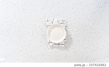 Flat lay. Empty a white plate with a kitchen towel on the white kitchen counter. Flat lay. Empty a white plate with a kitchen towel on the white kitchen counter. 107420862