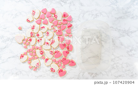 Flat lay. Storing heart-shaped sugar cookies with pink and white royal icing in a large plastic container. Flat lay. Storing heart-shaped sugar cookies with pink and white royal icing in a large plastic container. 107420904