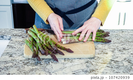 Large organic asparagus stalks are being sliced in a modern white kitchen, in preparation for steaming. Large organic asparagus stalks are being sliced in a modern white kitchen, in preparation for steaming. 107420939