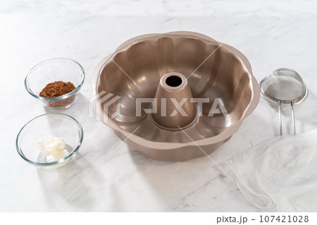 Greasing metal bundt cake pan with vegetable shortening and cocoa powder to bake gingerbread bundt cake with caramel filling. 107421028