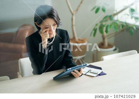 タブレット端末を見る喪服の女性 107421029