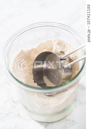 Measuring cup inside glass jar filled with all-purpose flour. 107421188